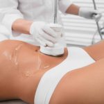 Beautiful woman having cavitation, procedure removing cellulite on her belly at beauty clinic